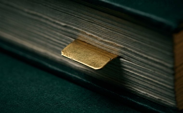 Detalhe de um marcador dourado saindo do meio de uma pilha de autos
